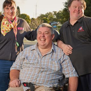Three people with a disability standing outside their Aruma disability service