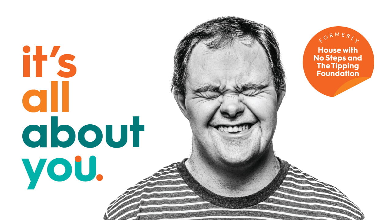 Man with down syndrome smiling and the text written in rainbow colours saying 'it's all about you'