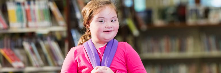 Girl with Down syndrome standing in a library with a backpack