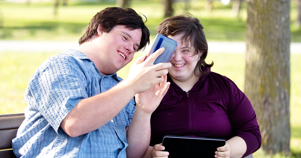 Couple with Down Syndrome in a park with mobile phone.