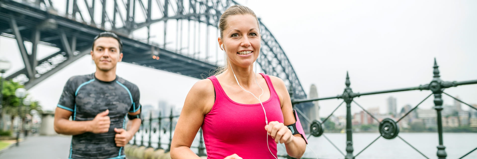 Woman wearing a pink top running with a man in a grey top near the Sydney Harbour Bridge