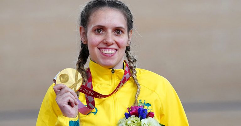 Amanda wearing a gold jacket, smiling and holding up a gold metal