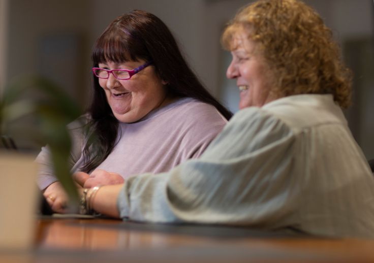 customer survey image of a customer with a support worker sitting at a desk together and smiling..